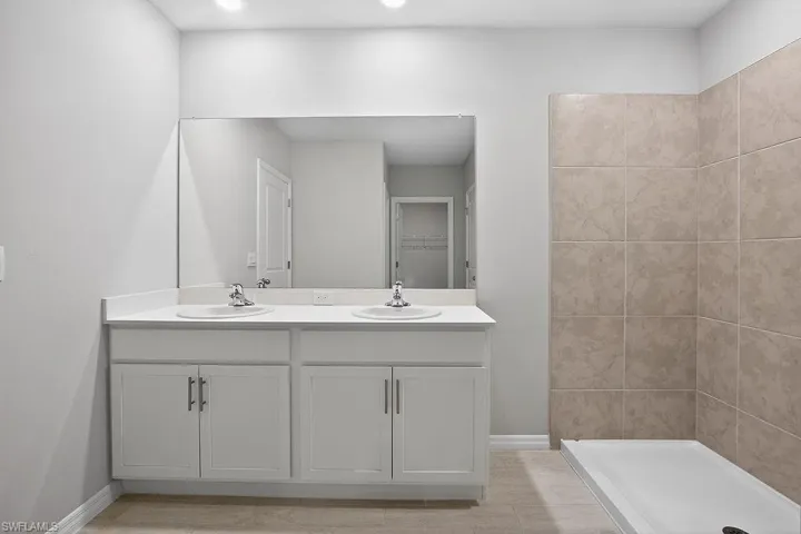 Full bath featuring double vanity, a walk in closet, and a stall shower