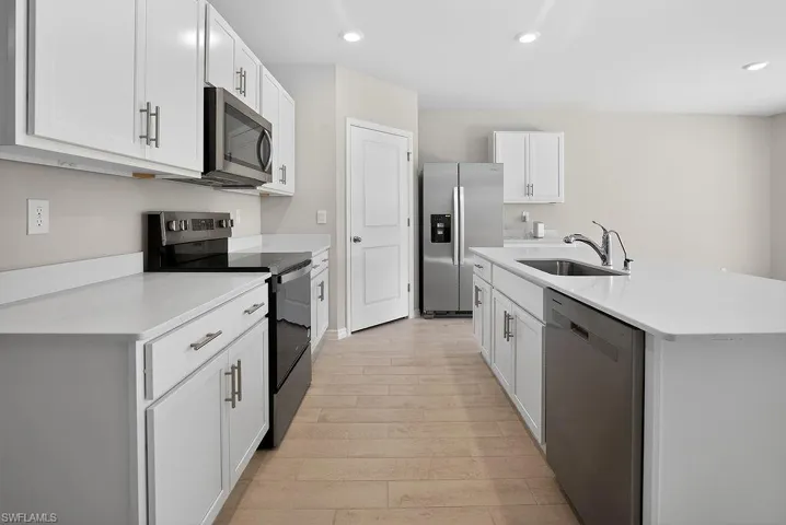 Kitchen with appliances with stainless steel finishes, white cabinetry, a kitchen island with sink, recessed lighting, and light wood-style flooring
