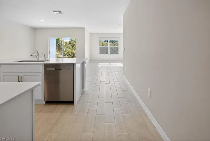 Kitchen with stainless steel dishwasher, white cabinetry, open floor plan, light wood finished floors, and light stone countertops