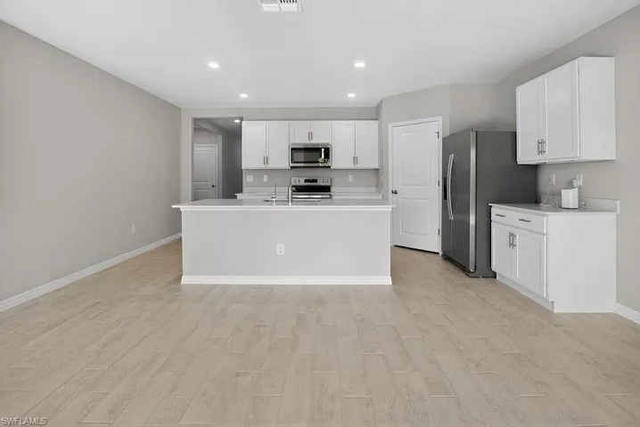 Kitchen featuring white cabinetry, recessed lighting, light wood finished floors, stainless steel appliances, and a kitchen island with sink