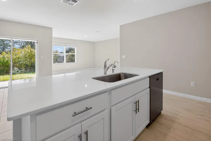 Kitchen with white cabinets, dishwasher, light wood-style floors, an island with sink, and light stone countertops
