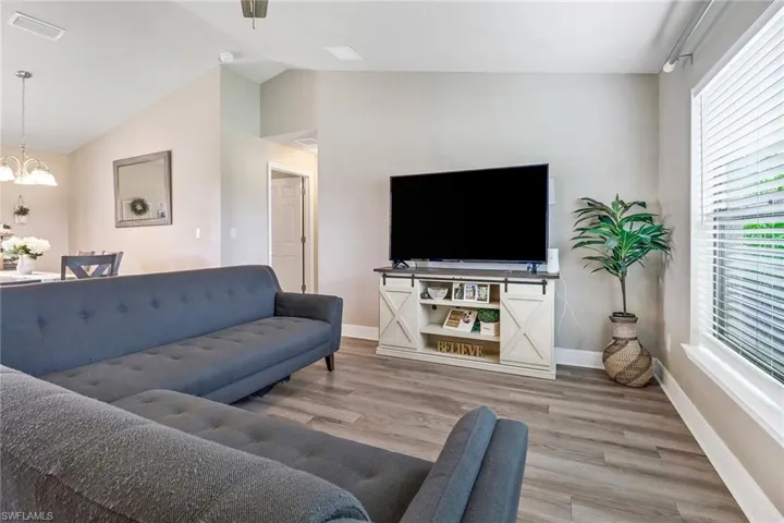 Living room with rail lighting, hardwood / wood-style flooring, a notable chandelier, and vaulted ceiling