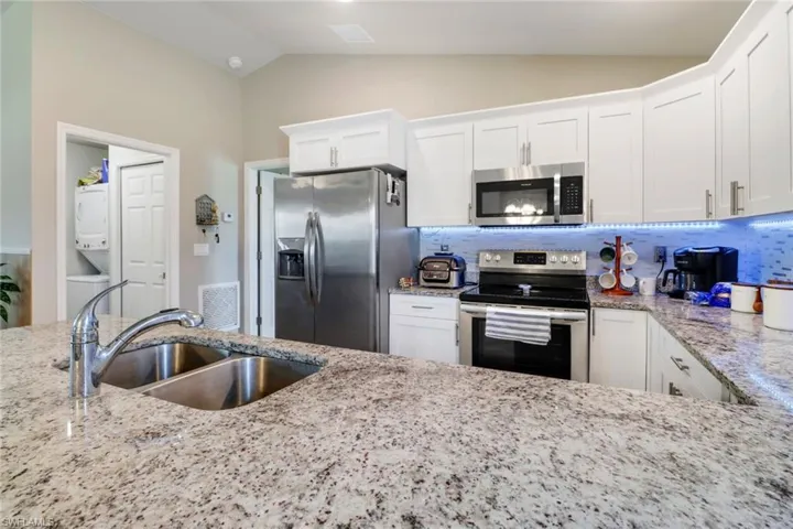 Kitchen with appliances with stainless steel finishes, white cabinets, vaulted ceiling, sink, and stacked washer and clothes dryer