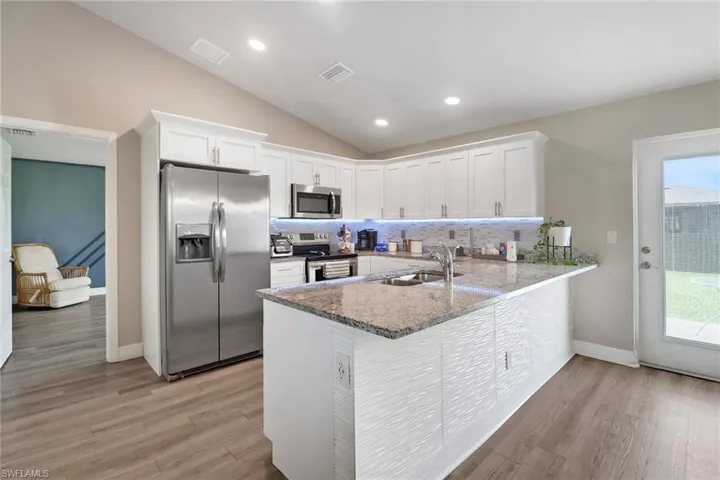 Kitchen featuring appliances with stainless steel finishes, tasteful backsplash, kitchen peninsula, light wood-type flooring, and white cabinetry