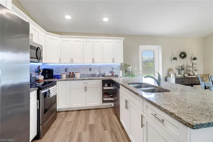 Kitchen with appliances with stainless steel finishes, light hardwood / wood-style flooring, white cabinetry, and decorative backsplash
