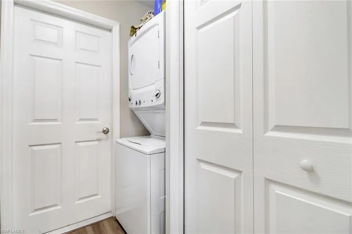 Laundry room with stacked washer and clothes dryer and wood-type flooring
