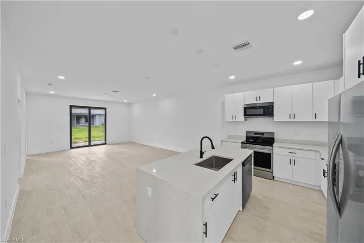 Kitchen with white cabinets, stainless steel appliances, light stone counters, recessed lighting, and wood tiled floors