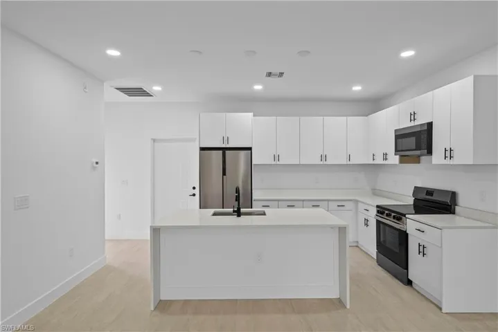 Kitchen with stainless steel appliances, light stone countertops, recessed lighting, white cabinetry, and light wood finished floors