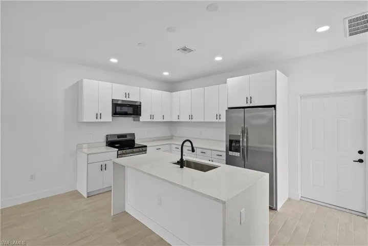 Kitchen with stainless steel appliances, light stone countertops, light wood finished floors, white cabinetry, and recessed lighting