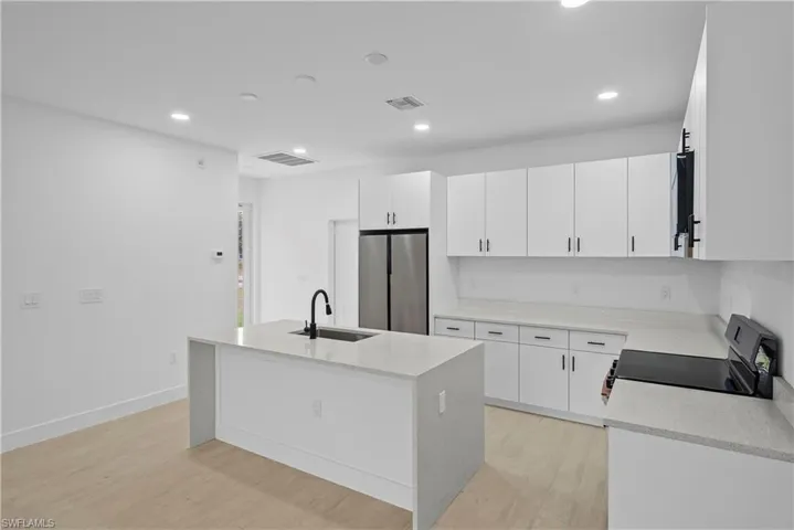 Kitchen with light stone countertops, electric range, a center island with sink, freestanding refrigerator, and recessed lighting