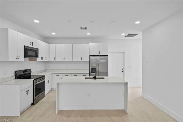 Kitchen with stainless steel appliances, white cabinets, recessed lighting, light stone counters, and light wood-style floors