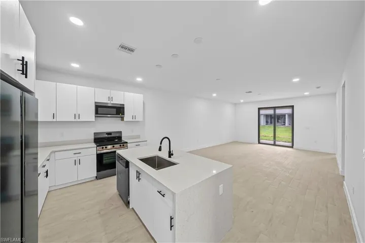 Kitchen featuring stainless steel appliances, white cabinetry, a kitchen island with sink, light wood finished floors, and recessed lighting