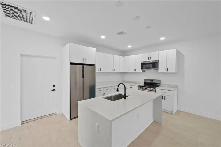 Kitchen with white cabinetry, stainless steel appliances, light stone counters, light wood-type flooring, and recessed lighting