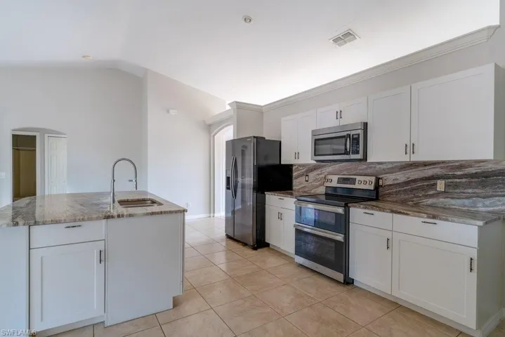 Kitchen featuring stainless steel appliances, white cabinets, backsplash, a center island with sink, and vaulted ceiling