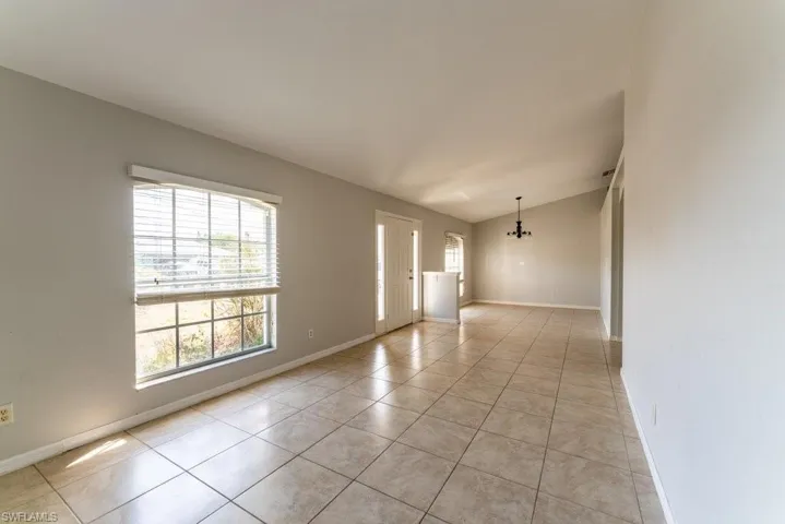 Empty room with light tile patterned flooring, vaulted ceiling, and a chandelier