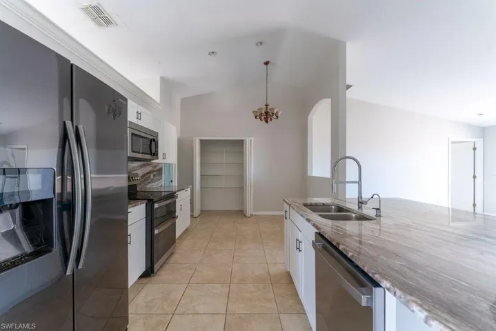 Kitchen featuring stainless steel appliances, white cabinets, dark stone countertops, lofted ceiling, and light tile patterned flooring