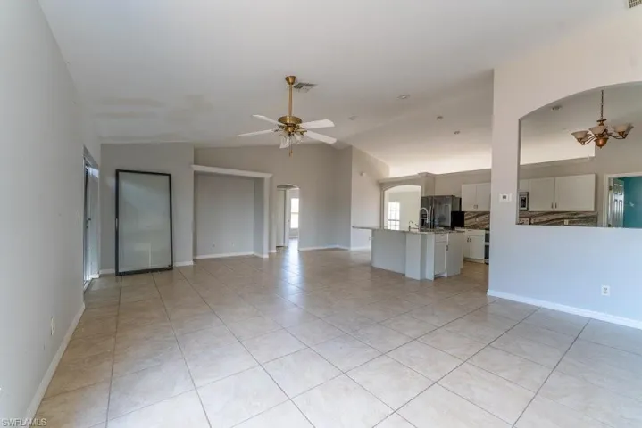 Unfurnished living room featuring arched walkways, light tile patterned floors, vaulted ceiling, and a ceiling fan