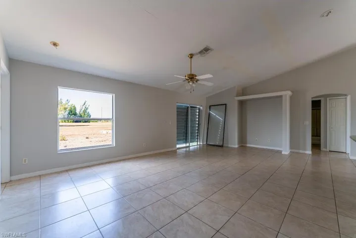 Empty room featuring arched walkways, light tile patterned floors, ceiling fan, and lofted ceiling