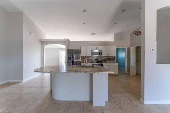 Kitchen featuring arched walkways, stainless steel appliances, white cabinets, and light tile patterned floors