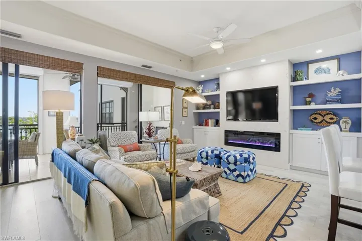 Living area featuring built in shelves, a ceiling fan, ornamental molding, a glass covered fireplace, and light wood-type flooring