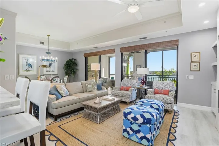 Living room with ornamental molding, a tray ceiling, a ceiling fan, light wood-style flooring, and hanging lights