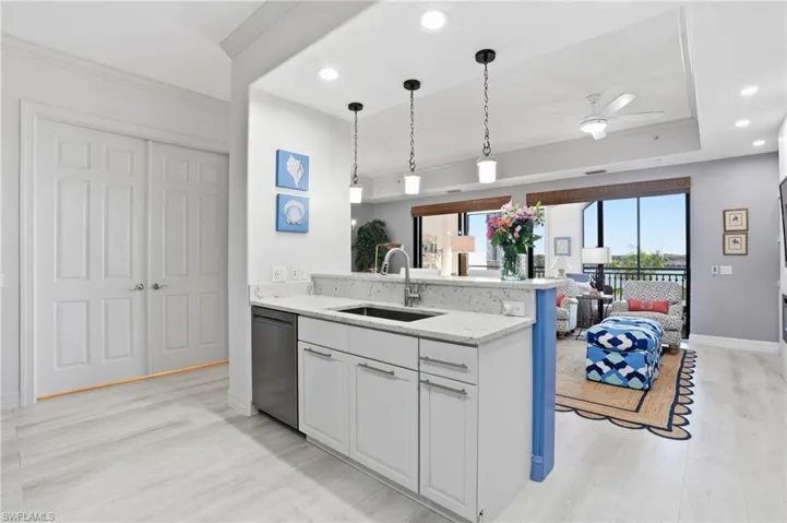 Kitchen featuring ornamental molding, hanging light fixtures, light stone counters, white cabinetry, and a ceiling fan