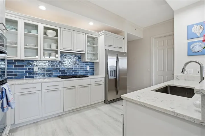 Kitchen with crown molding, light stone counters, stainless steel appliances, white cabinetry, and glass insert cabinets