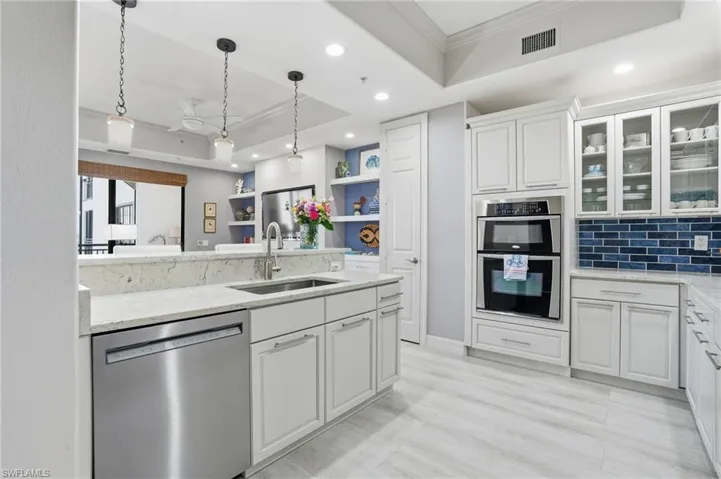 Kitchen with crown molding, a tray ceiling, hanging light fixtures, stainless steel appliances, and white cabinetry
