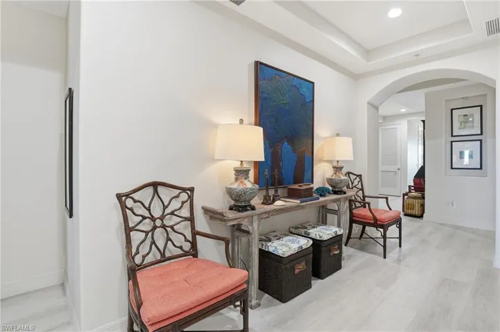 Living area with arched walkways, light wood-style floors, recessed lighting, and a raised ceiling