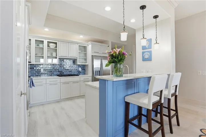 Kitchen featuring white cabinetry, decorative backsplash, ornamental molding, a kitchen breakfast bar, and light stone counters