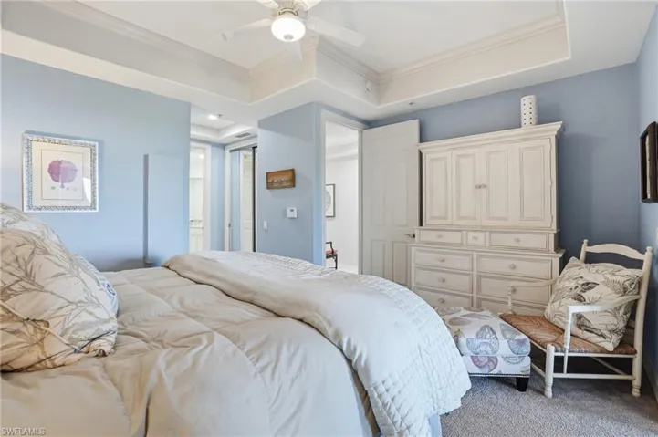Carpeted bedroom featuring ornamental molding, ceiling fan, and a raised ceiling