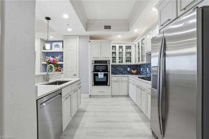 Kitchen featuring stainless steel appliances, ornamental molding, decorative light fixtures, glass insert cabinets, and white cabinets