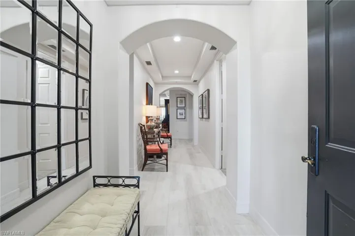 Hall featuring arched walkways, light wood-style flooring, recessed lighting, and a raised ceiling