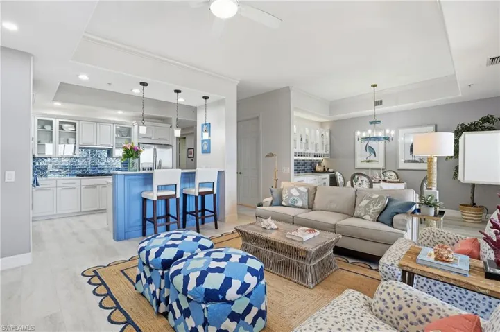 Living area featuring a raised ceiling, ornamental molding, light wood finished floors, a chandelier, and a ceiling fan