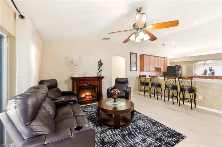 Living area with lofted ceiling, a warm lit fireplace, light tile patterned flooring, arched walkways, and a ceiling fan
