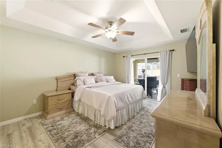 Bedroom with a raised ceiling, access to exterior, light wood-style flooring, and a ceiling fan