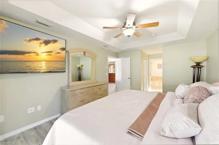 Bedroom with a raised ceiling, ensuite bathroom, a ceiling fan, and light wood-style floors