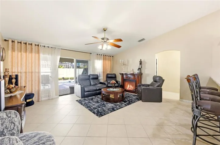 Living room with light tile patterned floors, a warm lit fireplace, arched walkways, and a ceiling fan