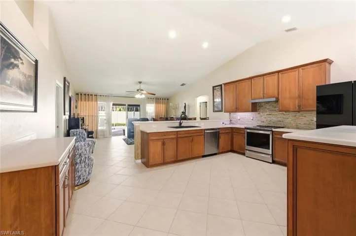 Kitchen featuring a peninsula, open floor plan, brown cabinetry, stainless steel appliances, and vaulted ceiling