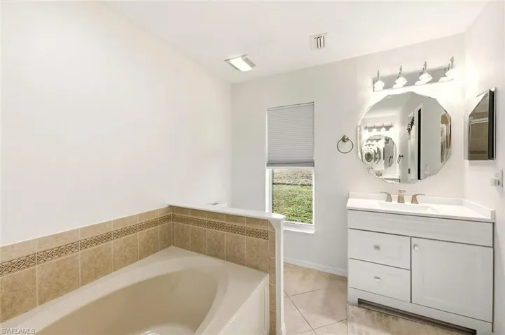Full bathroom featuring vanity, a garden tub, and light tile patterned floors