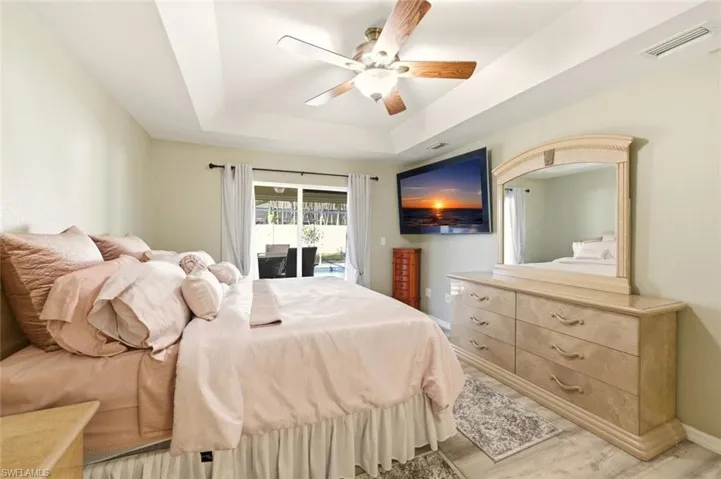 Bedroom featuring a tray ceiling, access to exterior, wood finished floors, and a ceiling fan
