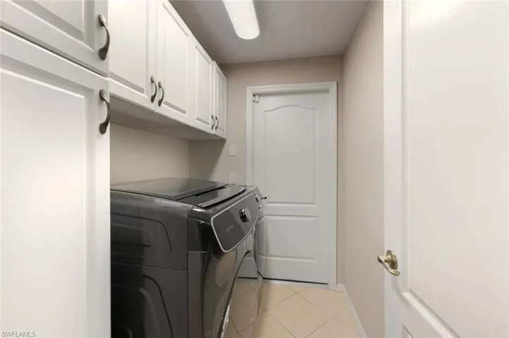 Laundry room featuring light tile patterned floors, separate washer and dryer, and cabinet space