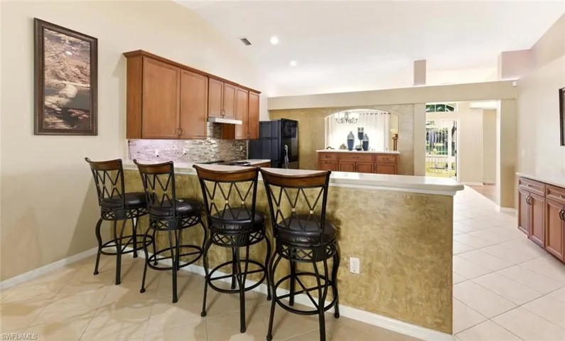 Kitchen featuring brown cabinetry, a peninsula, lofted ceiling, a kitchen breakfast bar, and tasteful backsplash
