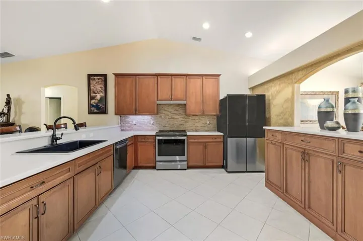 Kitchen featuring brown cabinetry, appliances with stainless steel finishes, lofted ceiling, decorative backsplash, and arched walkways