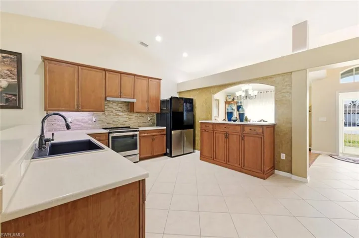 Kitchen featuring brown cabinetry, vaulted ceiling, stainless steel electric stove, light countertops, and recessed lighting