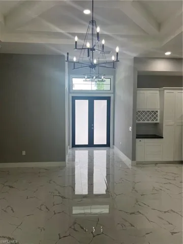 Tiled empty room with an inviting chandelier, french doors, and a tray ceiling