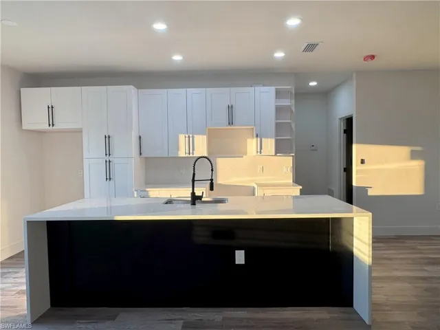 Kitchen with white cabinets, dark wood-type flooring, sink, backsplash, and a kitchen island with sink