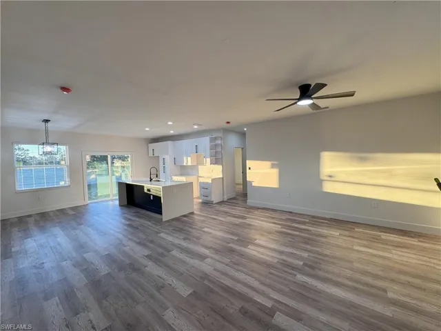 Kitchen featuring ceiling fan with notable chandelier, pendant lighting, dark hardwood / wood-style flooring, and a kitchen island with sink