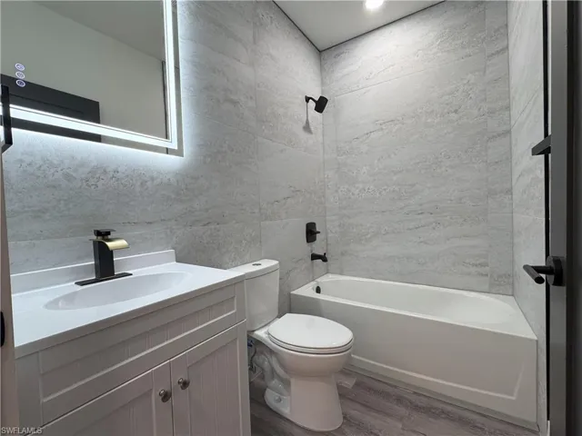 Full bathroom featuring toilet, hardwood / wood-style flooring, tile walls, vanity, and tub / shower combination