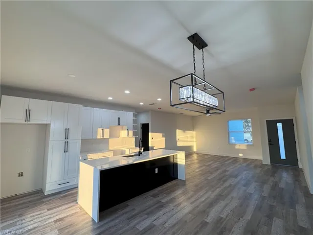 Kitchen with white cabinets, an island with sink, sink, hanging light fixtures, and hardwood / wood-style flooring